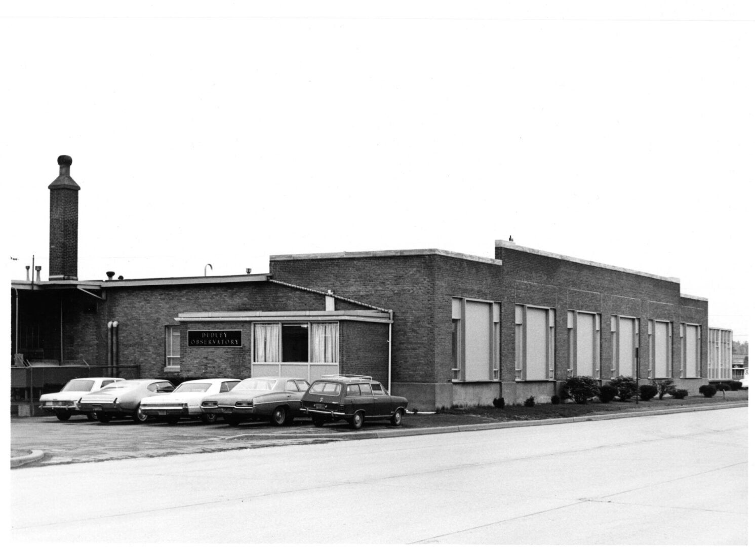 A black and white photo of a building with cars parked in front of it.