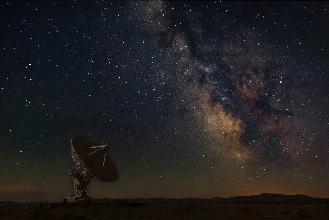 A satellite dish in the desert under a starry sky.