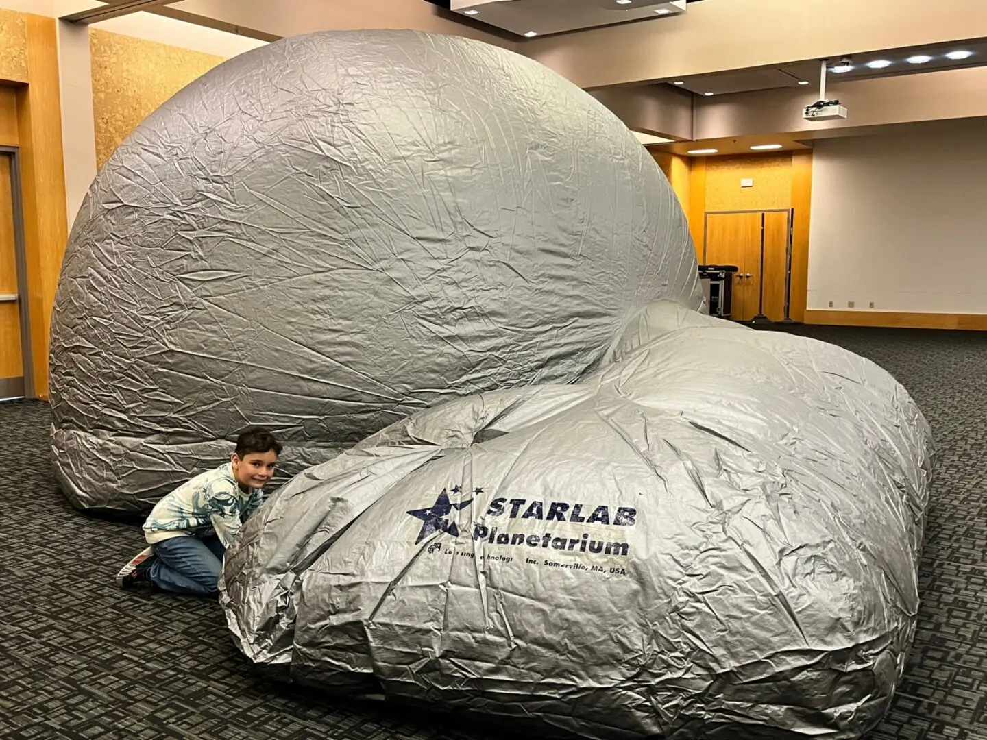 A child is standing next to a large silver ball in a room.