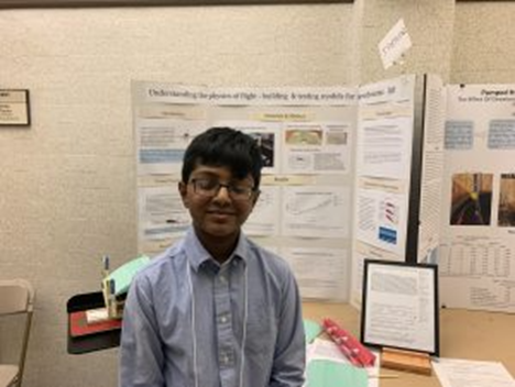 A boy standing in front of a poster at a science fair.