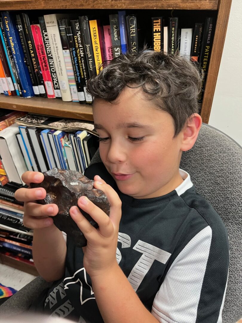 Boy holding a meteorite in front of bookshelves.